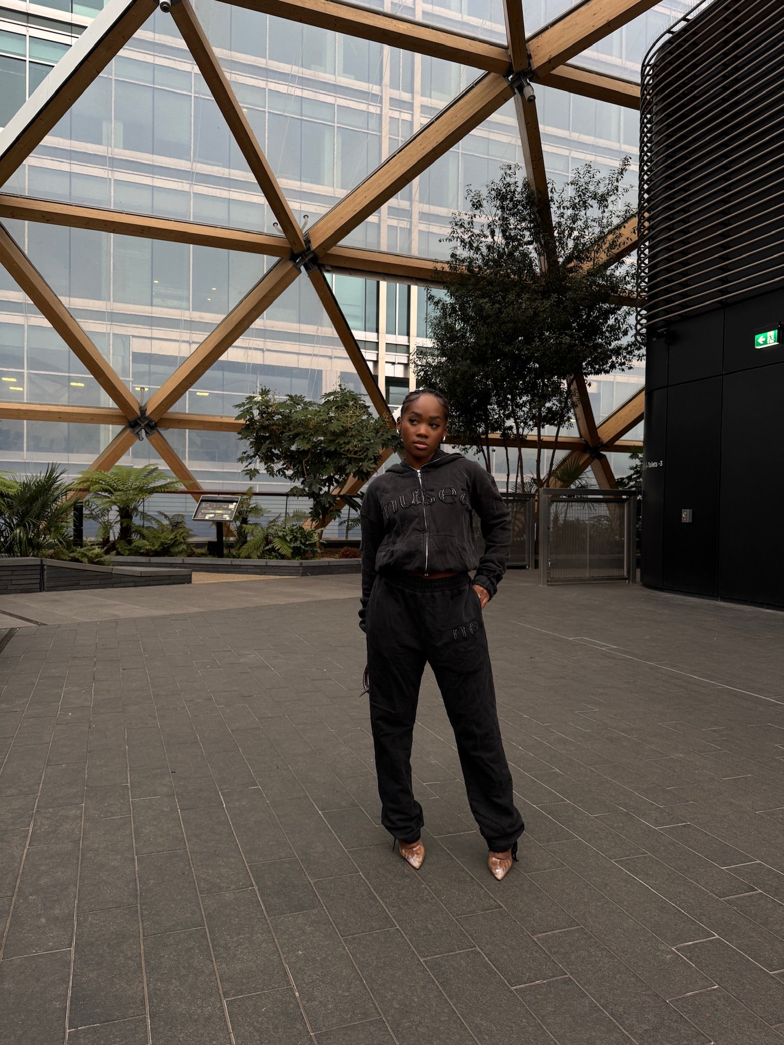Person standing in a modern outdoor setting with geometric wooden structure and glass building.