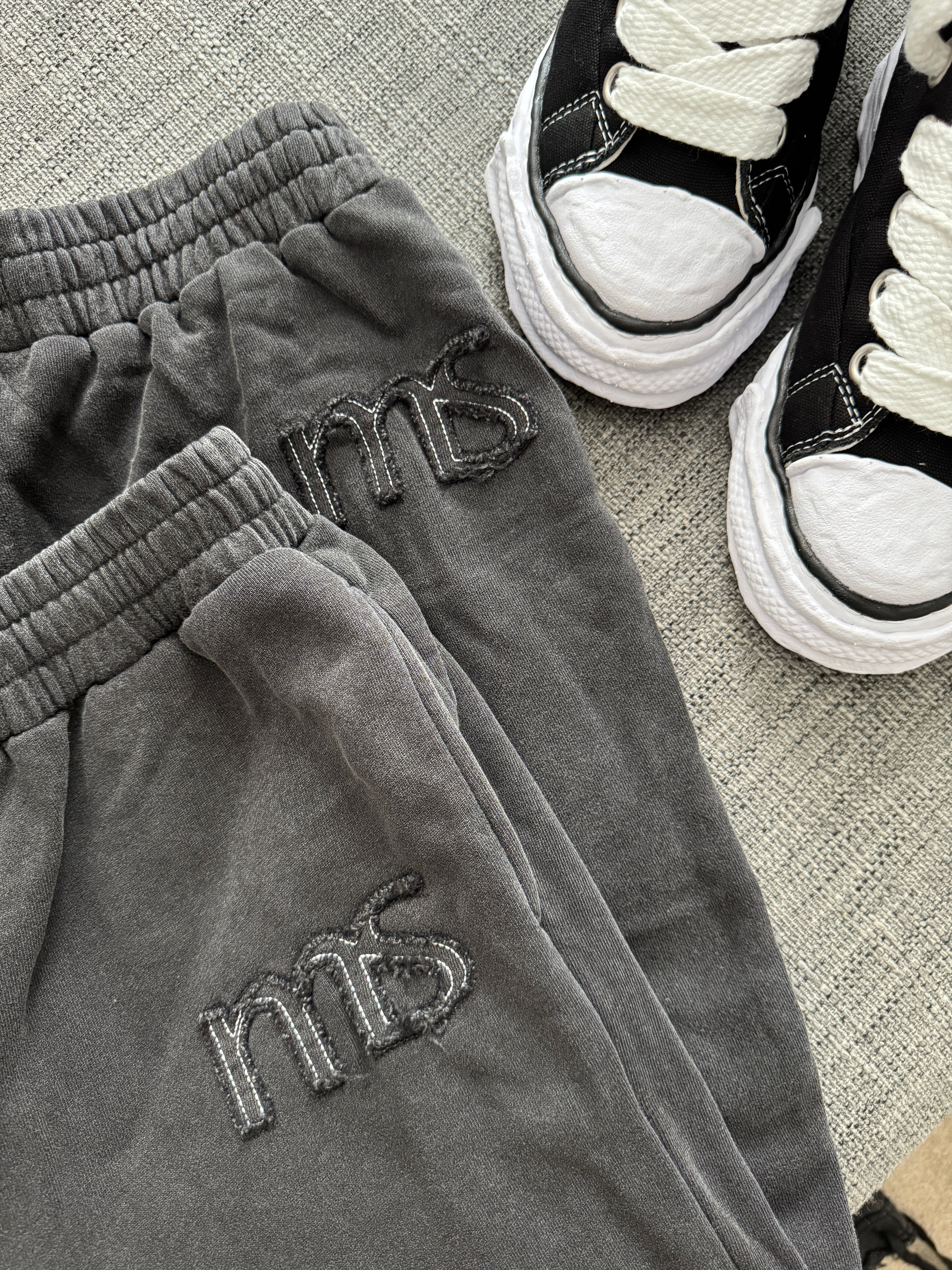 Gray sweatpants with 'ms' branding next to black sneakers on a textured surface