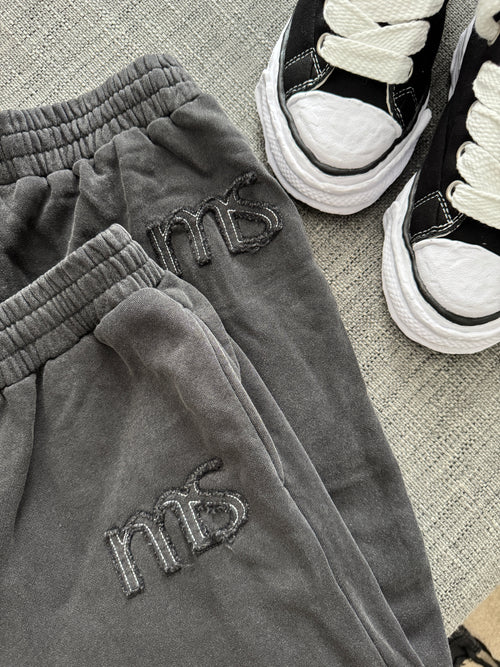 Gray sweatpants with 'ms' branding next to black sneakers on a textured surface