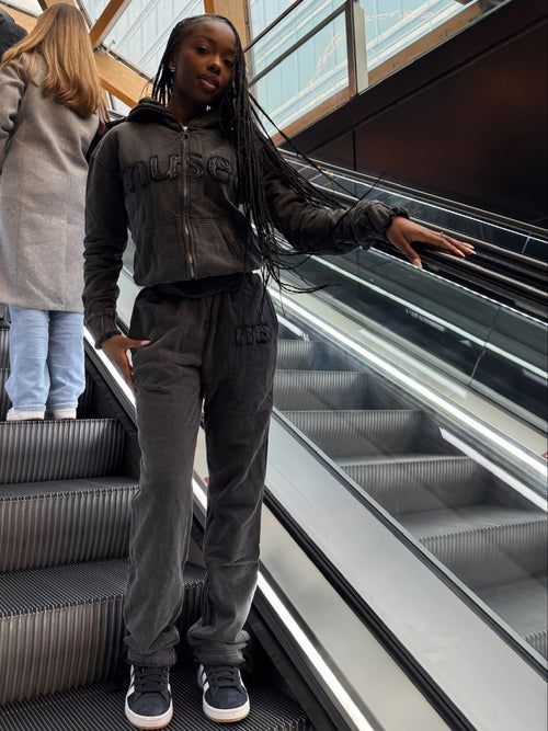 Person in a gray tracksuit standing on an escalator with a modern architectural background